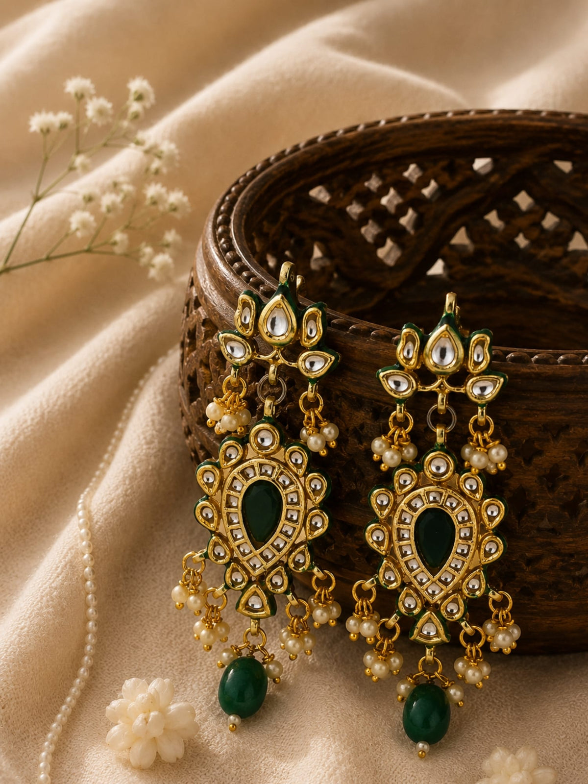 Kundan drop earrings with green stone and pearl detailing, gold-toned, laid flat