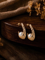 Hammered gold tone half hoop earrings with pearl ball accent, laid flat