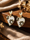 Gold-toned heart dangle earrings with black and white enamel floral detail, laid flat